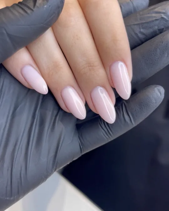 Manucure rose nude sur ongles amande, maintenue par des mains gantées