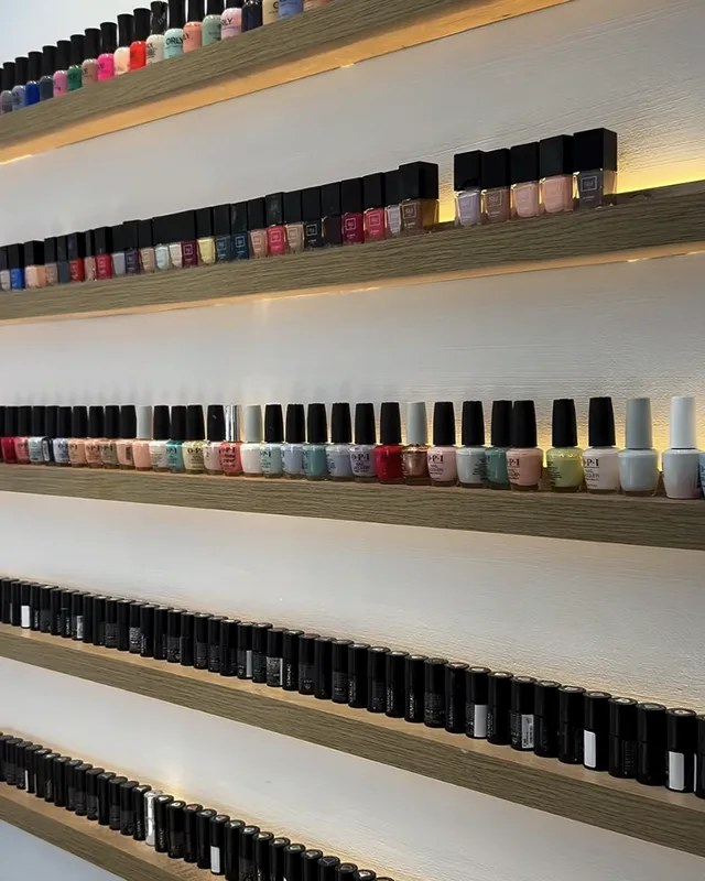 Le mur de vernis du salon, rangées de flacons colorés sur des étagères en bois rétroéclairées