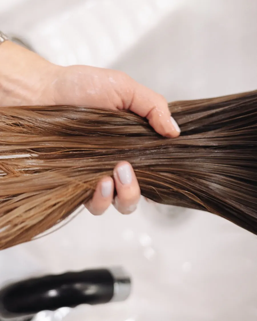Cheveux mouillés tenus au-dessus du bac de lavage, pendant un soin
